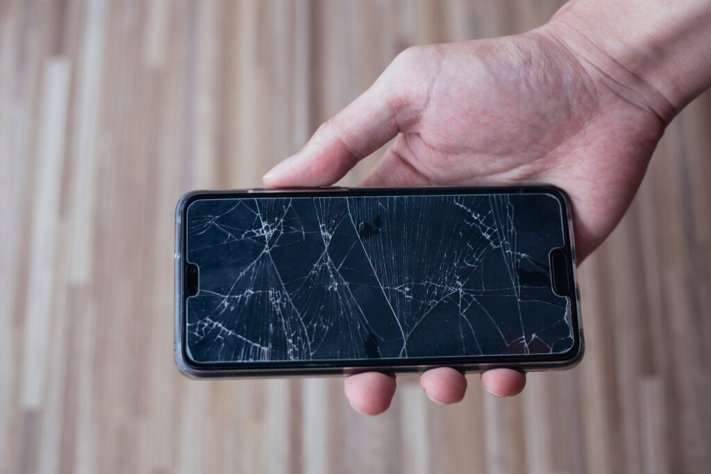 Close-up of human hand holding a broken and damaged glass of mobile phone from accident