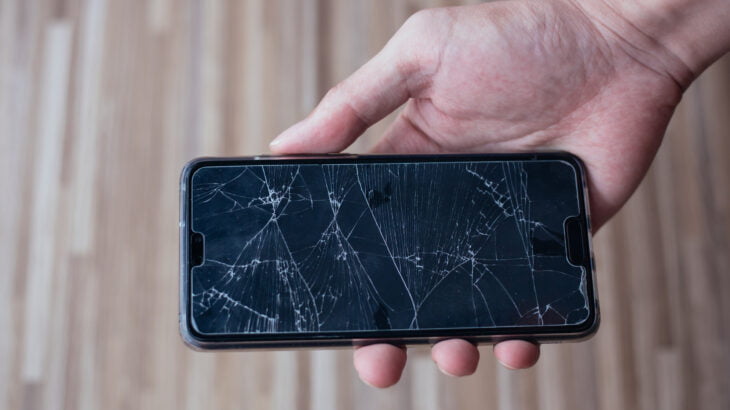 Close-up of human hand holding a broken and damaged glass of mobile phone from accident